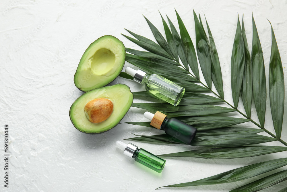 Composition with bottles of cuticle oil, avocado and palm leaf on light background