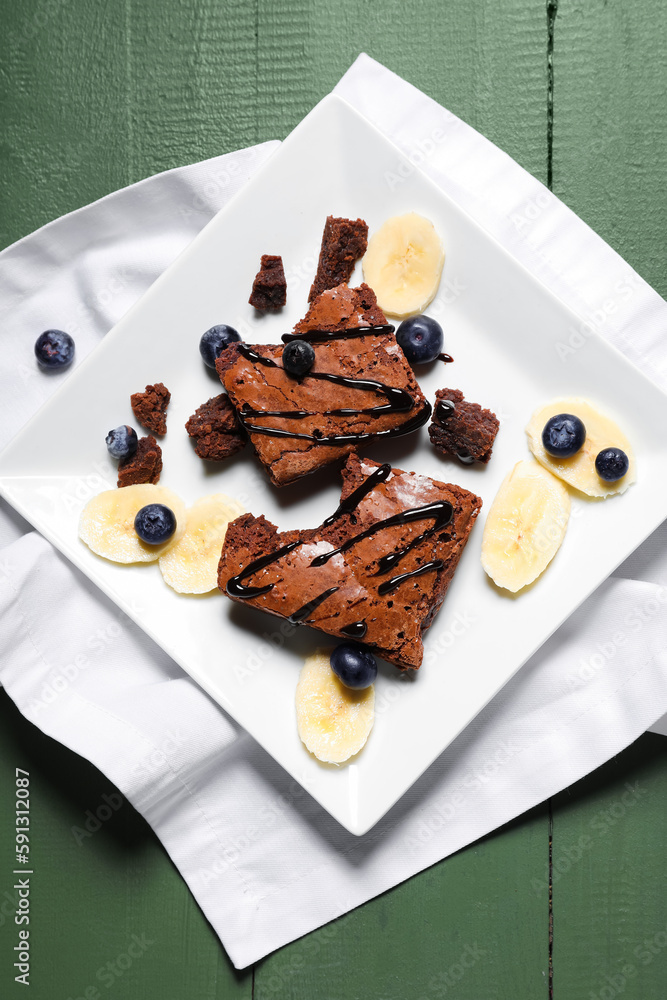 Plate with pieces of tasty chocolate brownie on green wooden background