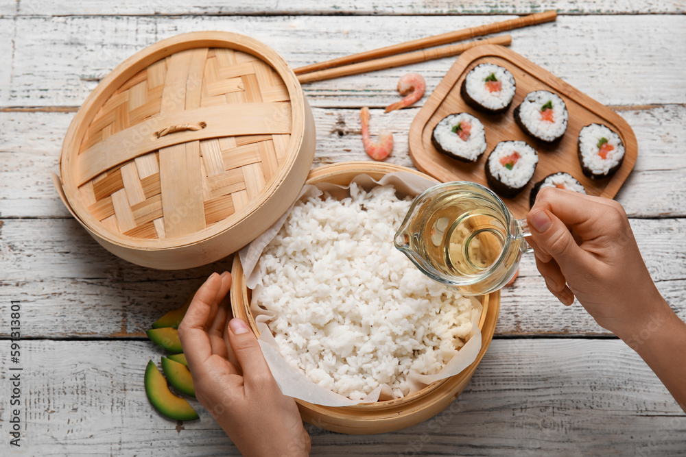 Woman adding vinegar into boiled rice on wooden table