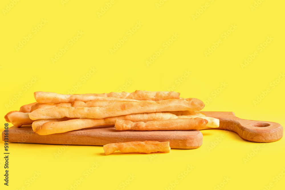 Wooden board with tasty Italian Grissini on yellow background