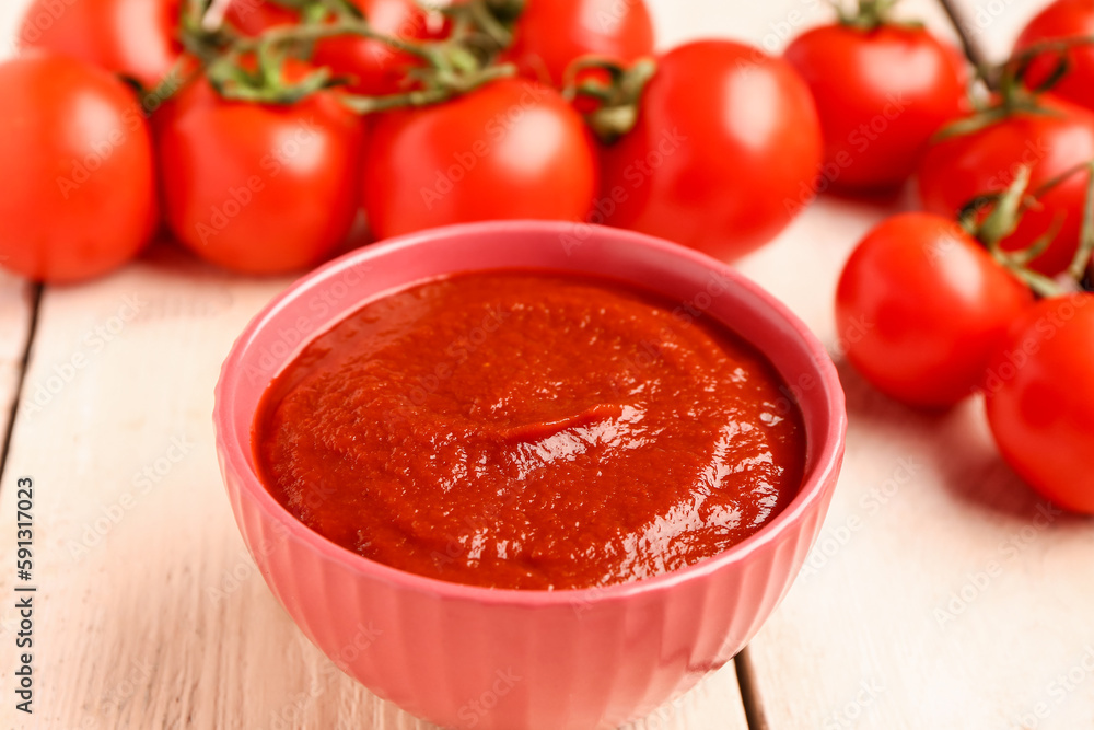 Bowl with tasty tomato paste on light wooden background, closeup