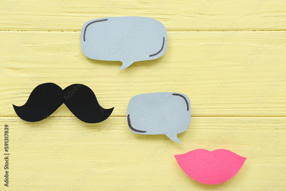 Paper mustache and lips with speech bubbles on yellow wooden background. Dialogue concept