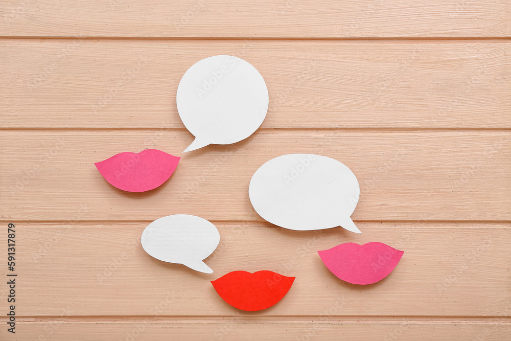 Paper lips with speech bubbles on beige wooden background. Dialogue concept