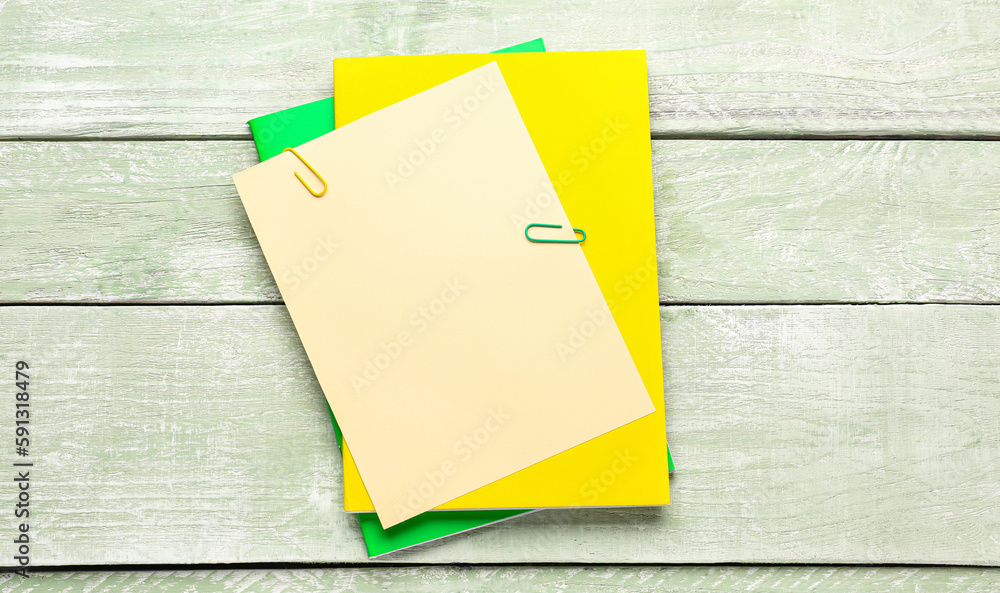 Beige, yellow and green paper sheets with clip on color wooden background