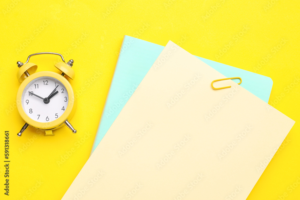 Paper sheets and clock on yellow background