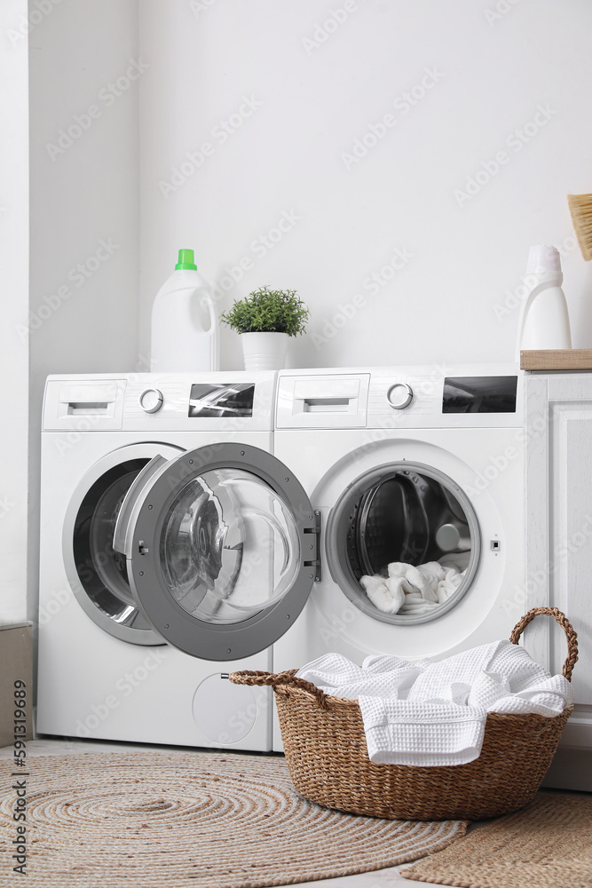 Modern washing machines with dirty clothes in laundry room