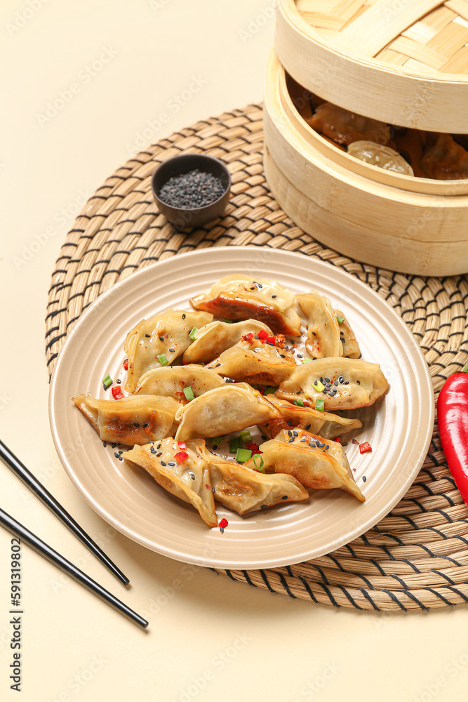 Plate with tasty Chinese jiaozi, red chili pepper and bamboo steamer on beige background