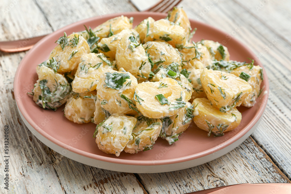 Plate of tasty Potato Salad with greens on light wooden background