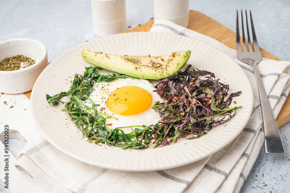 Plate with tasty fried egg, avocado and greens on light background