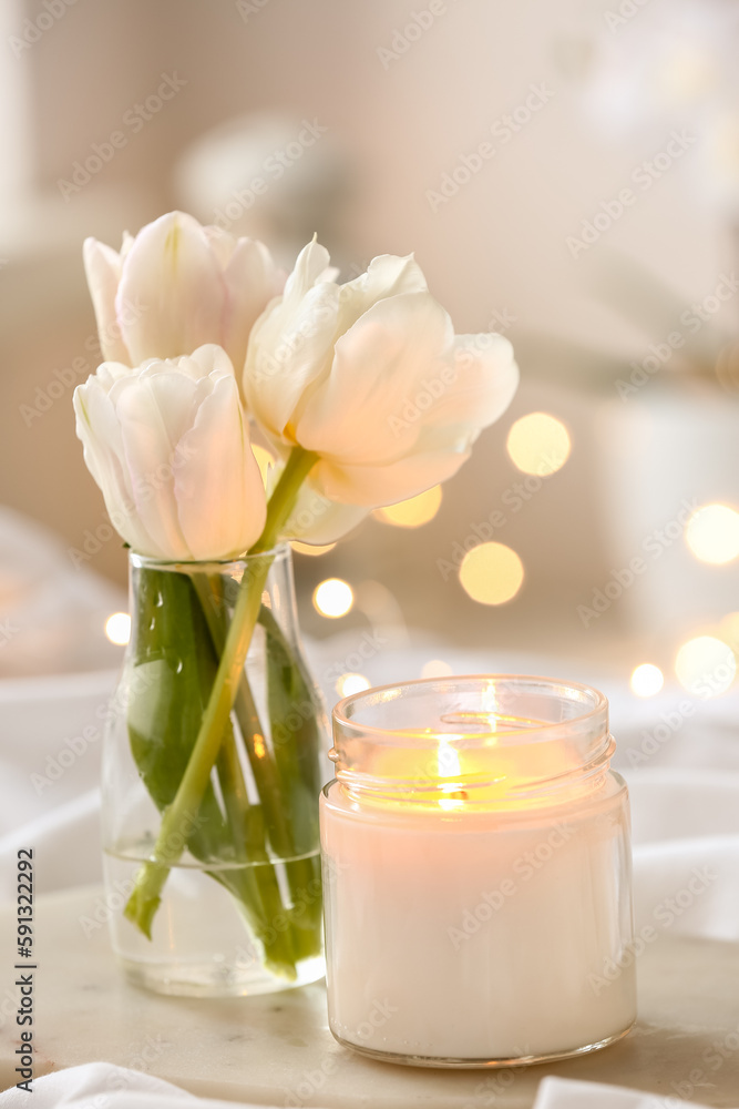 Burning candle and vase with tulips on bed, closeup