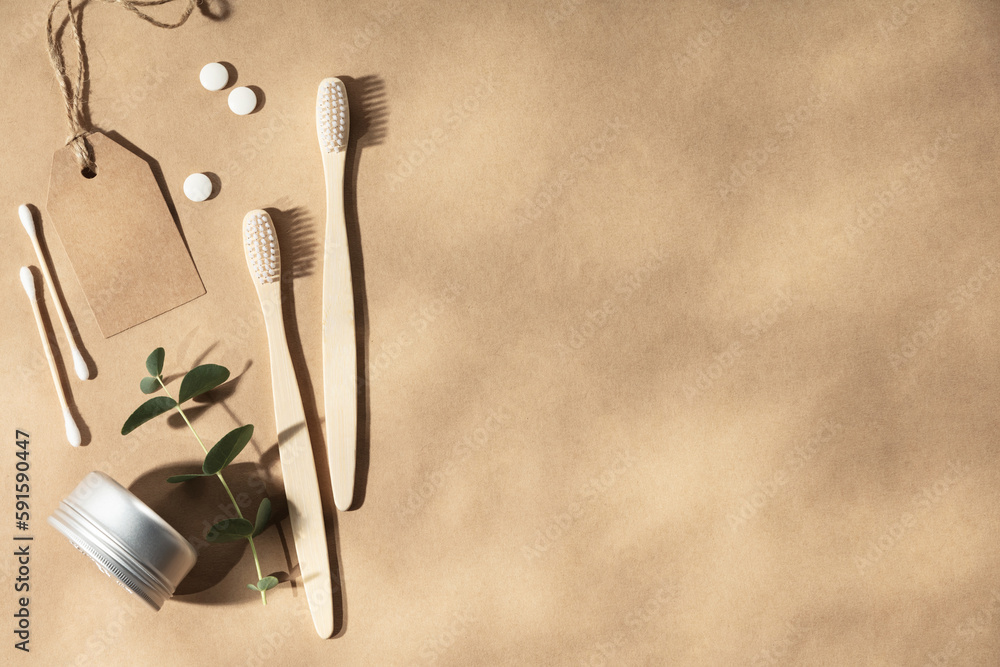 Two natural wooden toothbrushes on natural beige background with leaves shadows, flat lay, top view