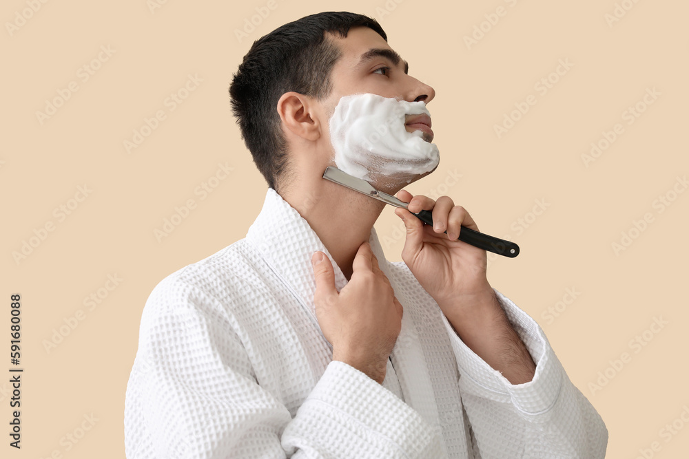 Young man shaving against beige background