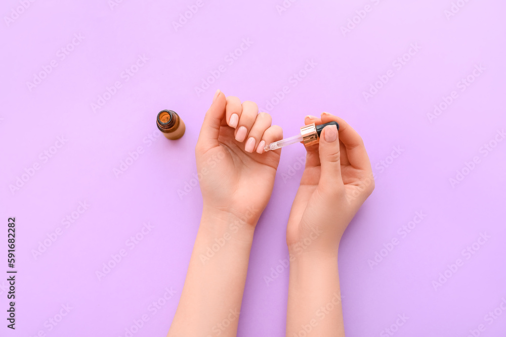 Female hands with bottle of cuticle oil on lilac background