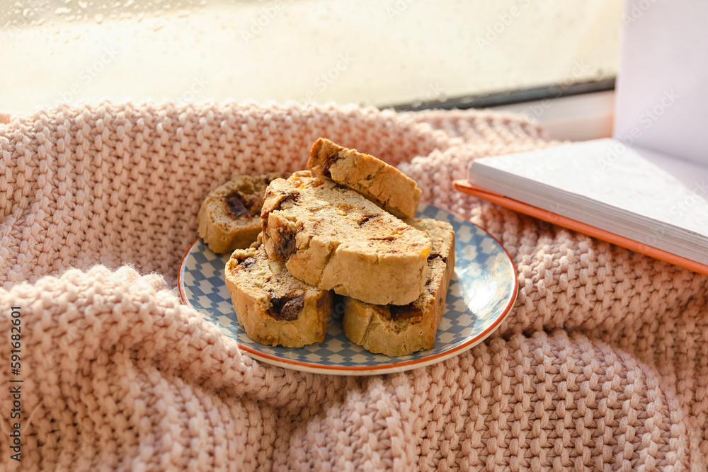 Plate with tasty biscotti cookies on knitted plaid near window