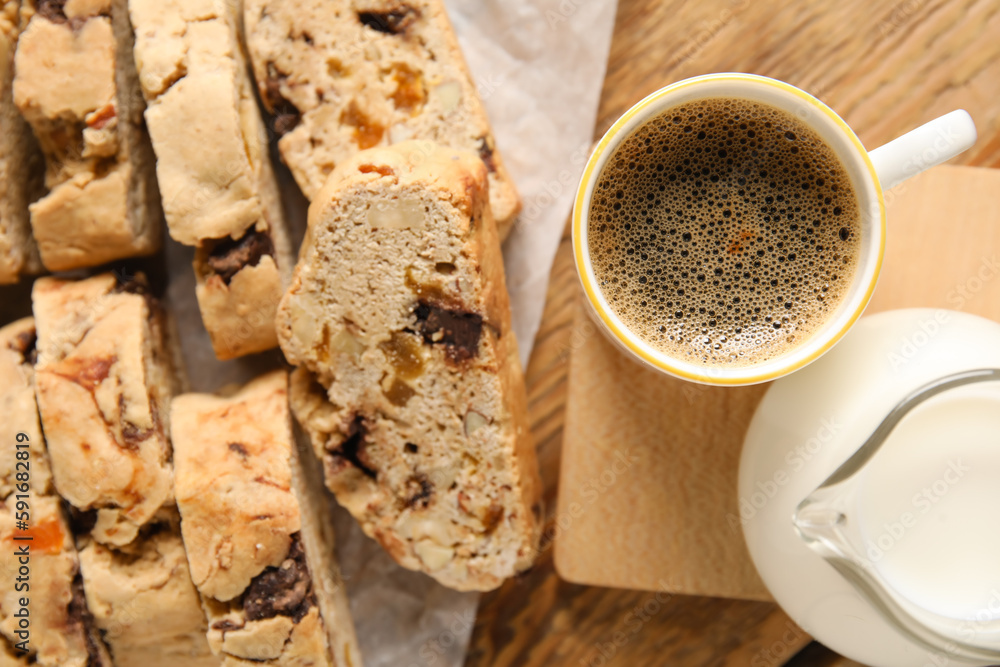 Delicious biscotti cookies, cup of coffee and milk in pitcher on wooden background