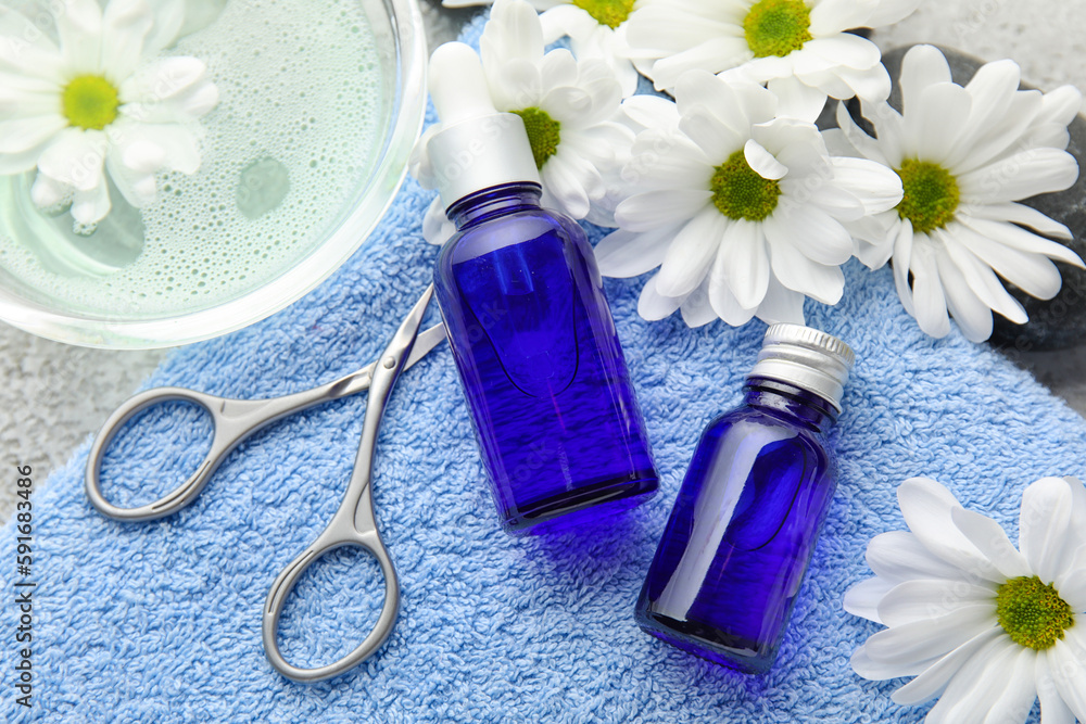 Bottles of cuticle oil, towel, manicure scissors and chamomile flowers, closeup