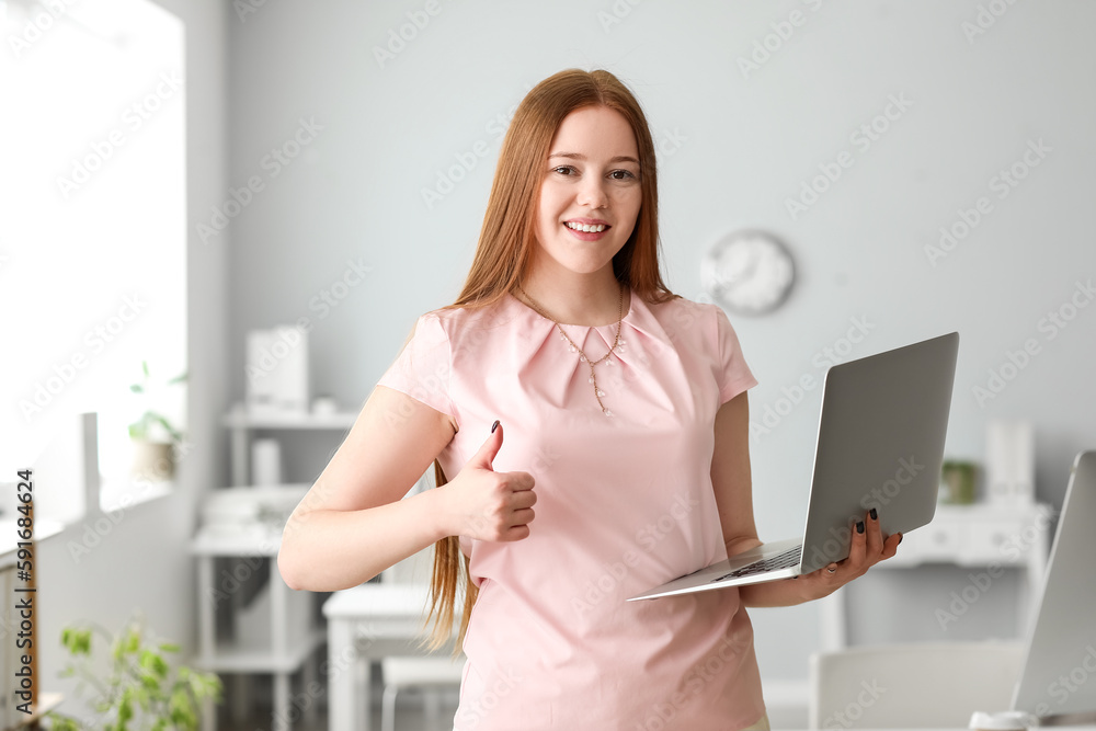 Female programmer with laptop showing thumb-up in office