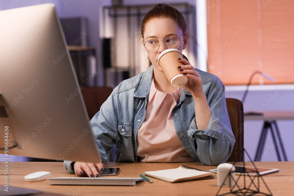 Female programmer drinking coffee in office at night