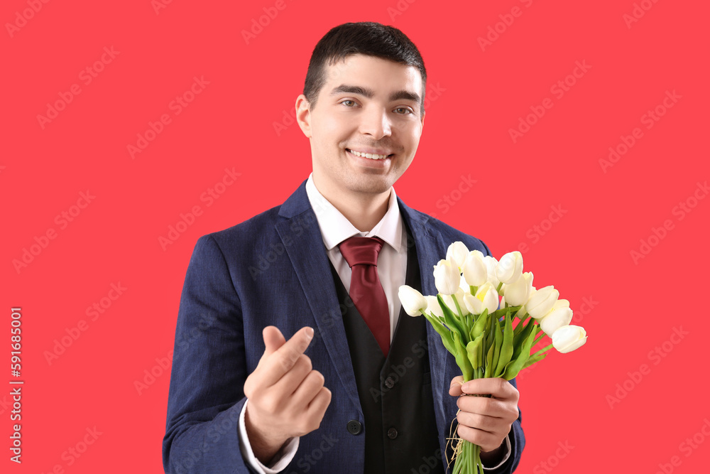 Young man with flowers making heart on red background