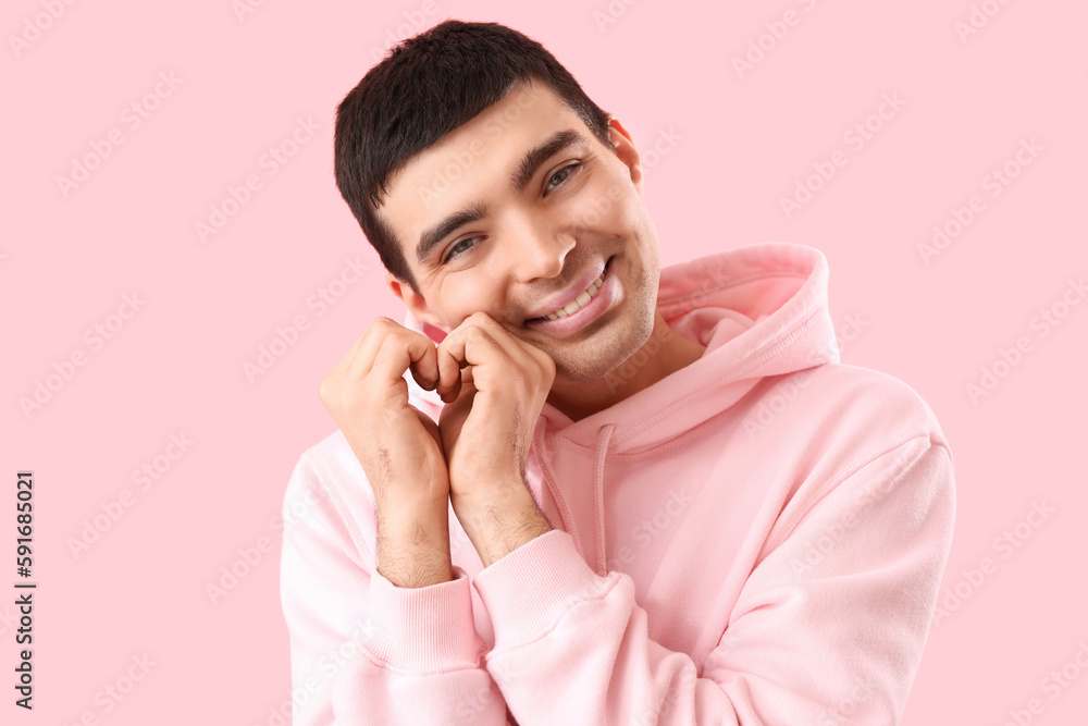 Young man making heart with his hands on pink background, closeup