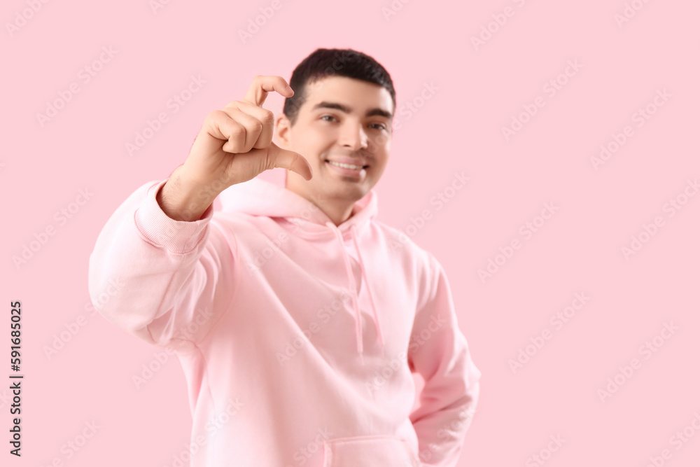 Young man making heart with his fingers on pink background