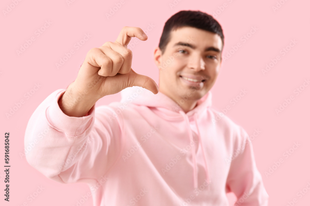 Young man making heart with his fingers on pink background, closeup