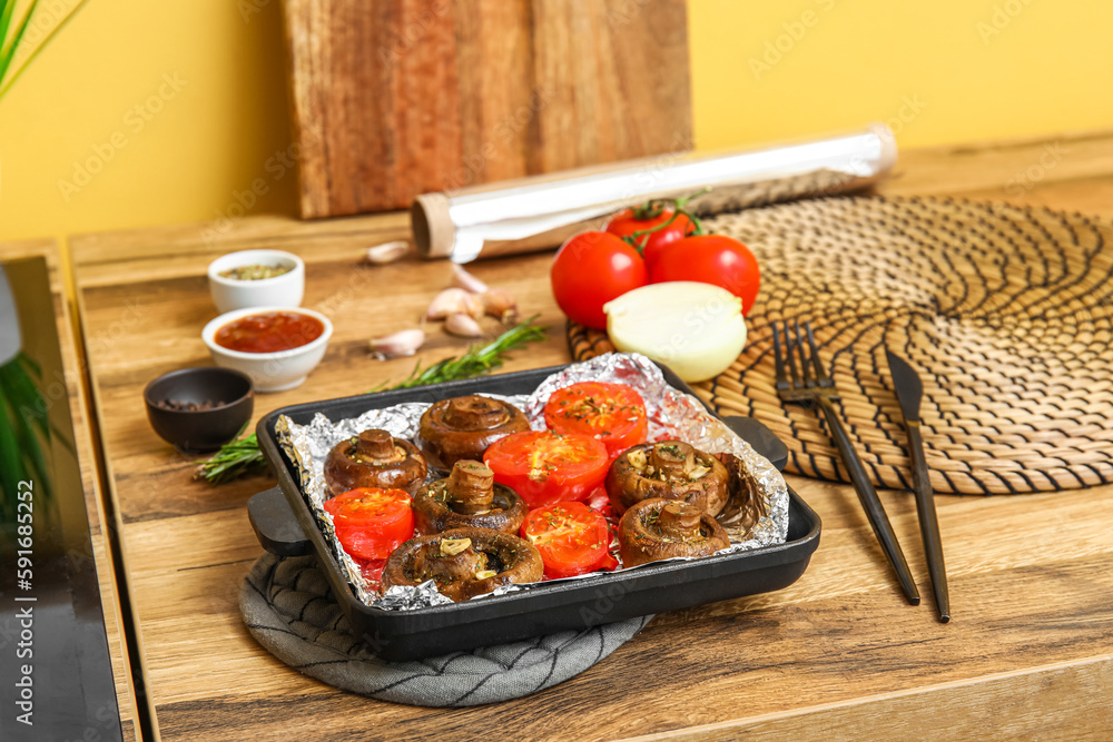 Baking dish with tasty baked mushrooms and tomatoes on wooden table in kitchen