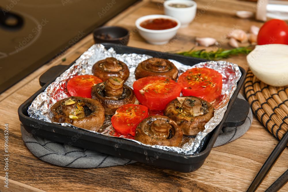 Baking dish with tasty baked mushrooms and tomatoes on wooden table in kitchen