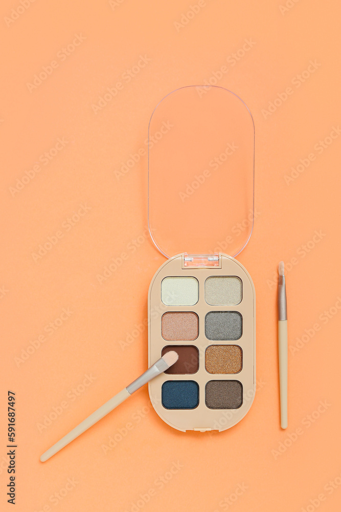 Palette of eyeshadows with brushes on color background