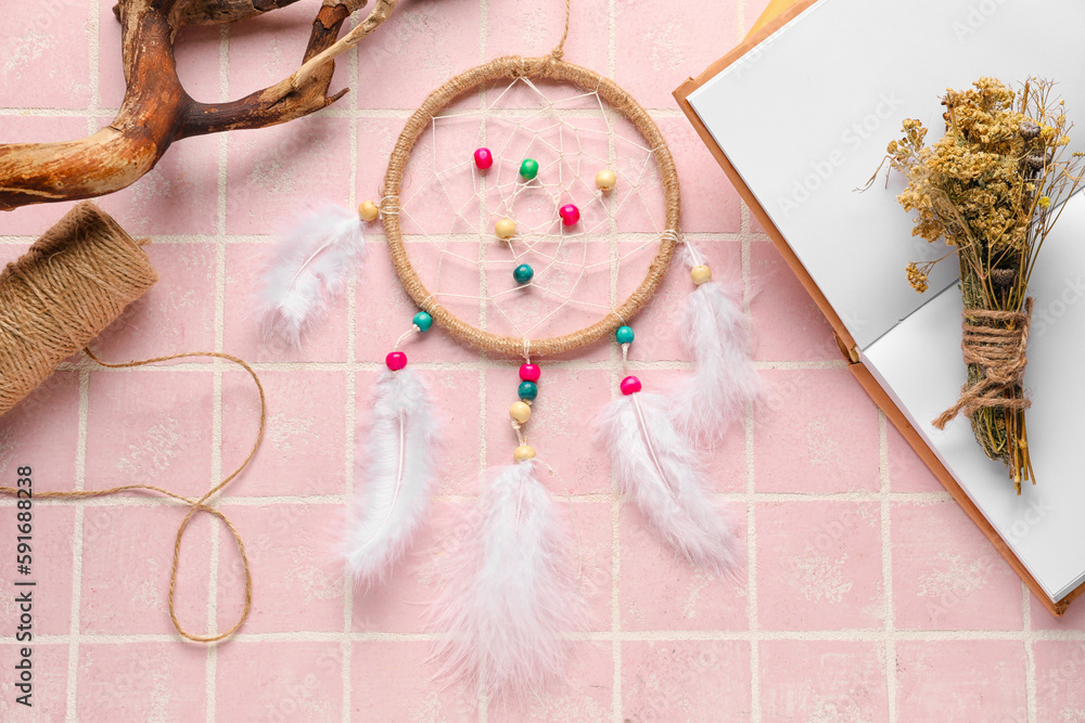 Dream catcher, tree branch, book and flowers on pink tile background