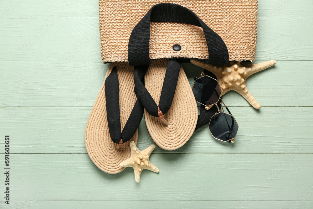 Bag with flip-flops, sunglasses and starfishes on green wooden background