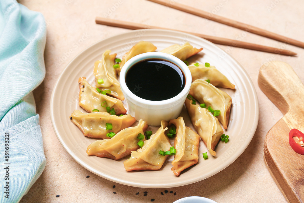 Plate with tasty Chinese jiaozi, green onion and sauce on beige background