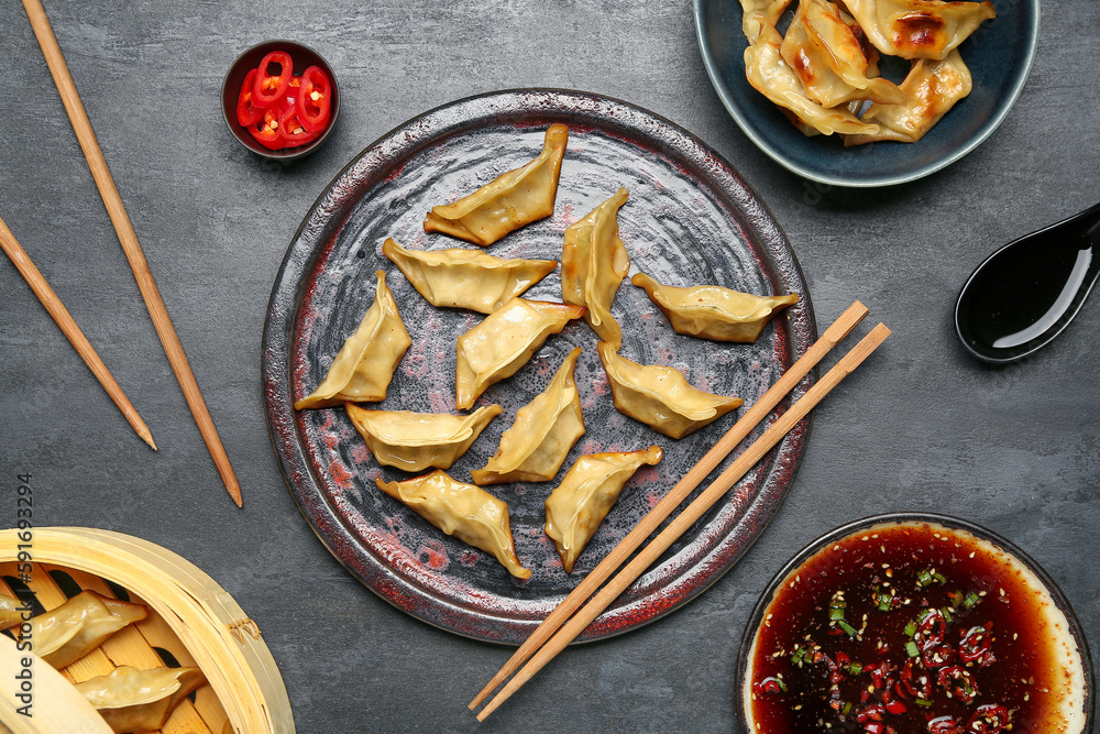 Plate with tasty Chinese jiaozi, bamboo steamer and sauce on black background