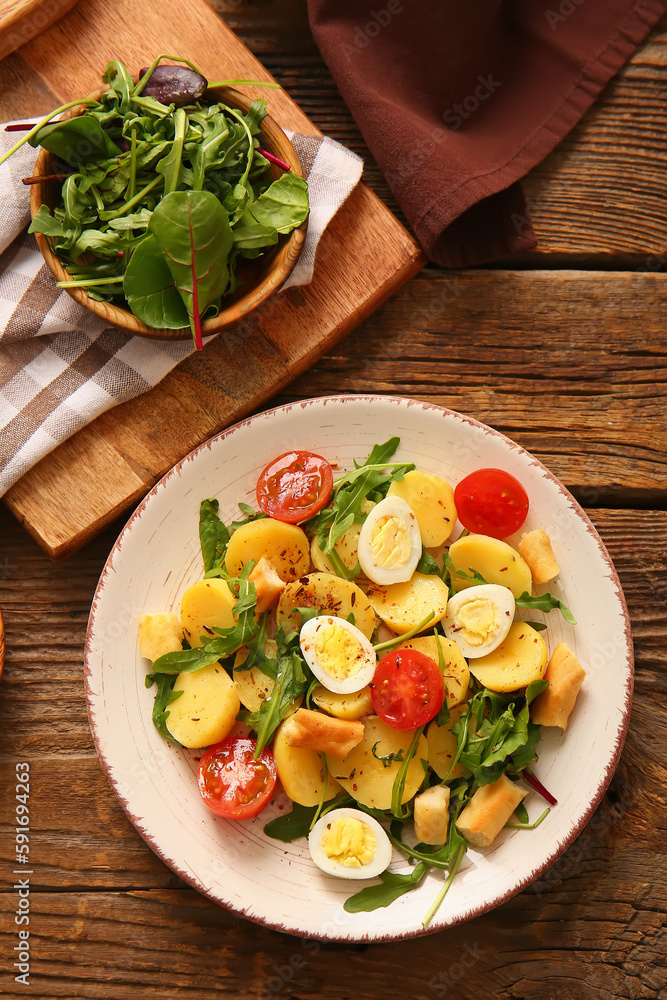 Plate of tasty potato salad with eggs and tomatoes on wooden background, top view