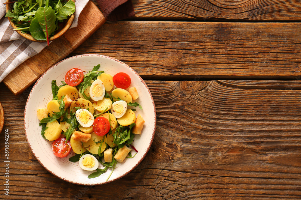 Plate of tasty potato salad with eggs and tomatoes on wooden background, top view