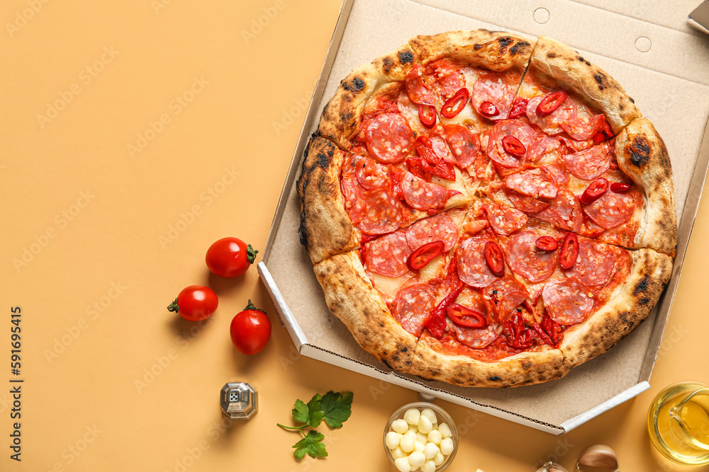 Cardboard box with delicious pepperoni pizza and ingredients on orange background