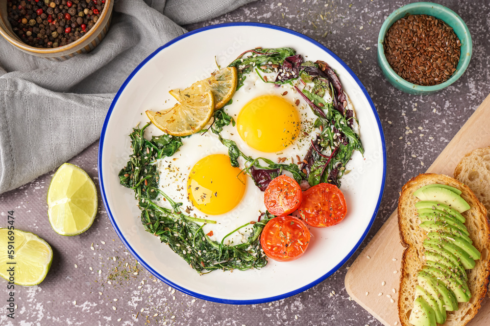 Plate with tasty fried eggs, salad and avocado sandwich on grey background