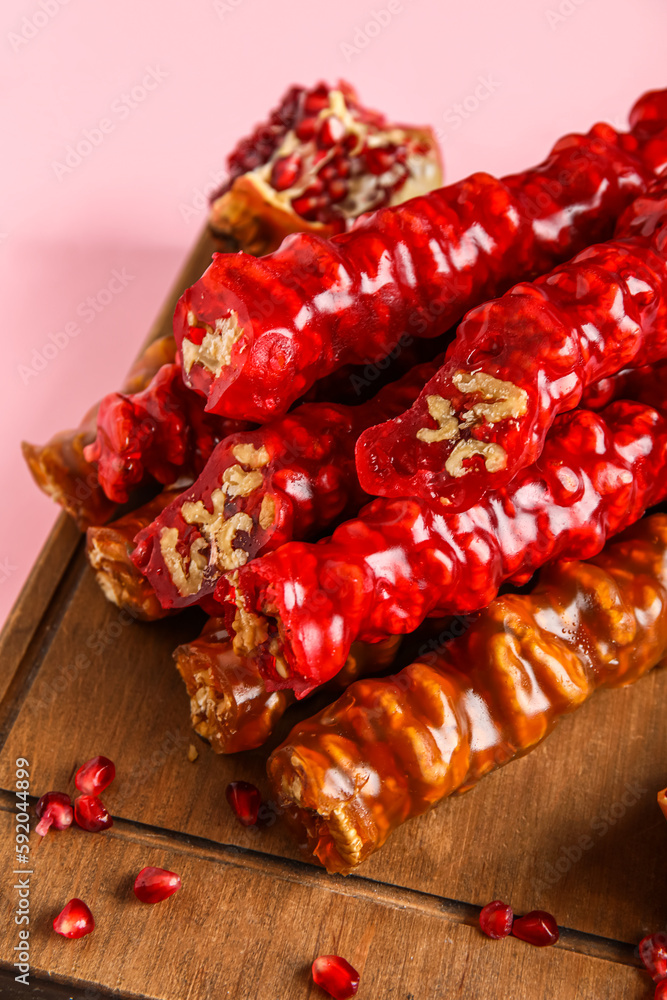 Board with delicious churchkhela and pomegranate on pink background