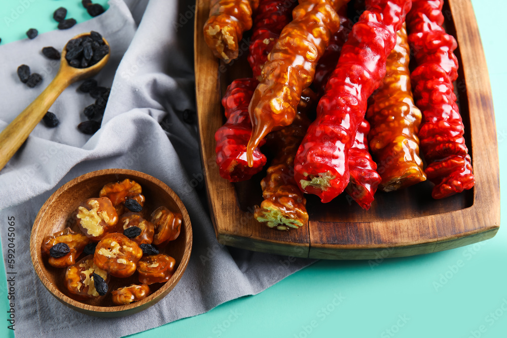 Board and bowl with delicious churchkhela on turquoise background