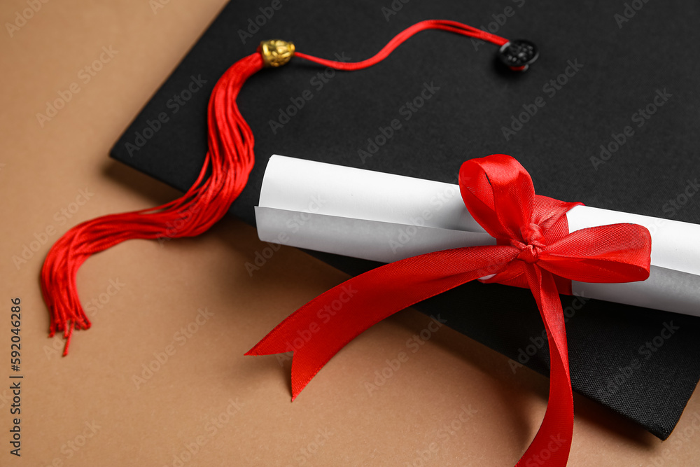 Diploma with red ribbon and graduation hat on brown background