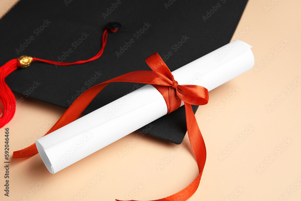 Diploma with red ribbon and graduation hat on beige background