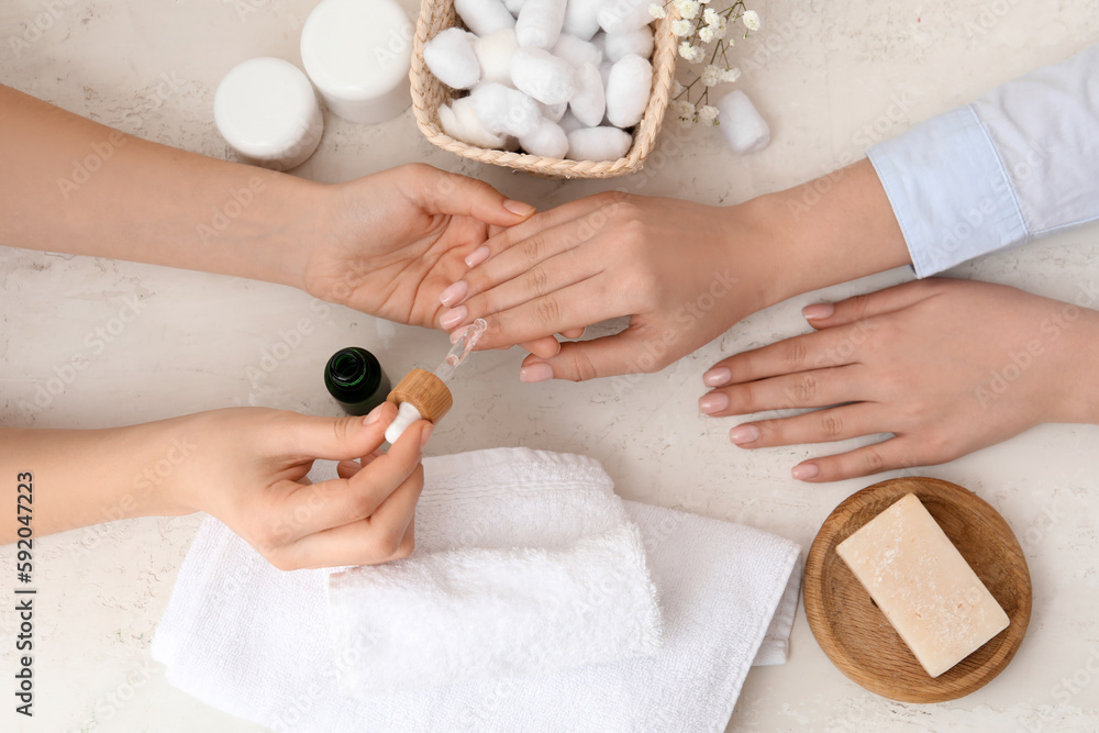 Manicure master applying cuticle oil onto female fingernails on light background