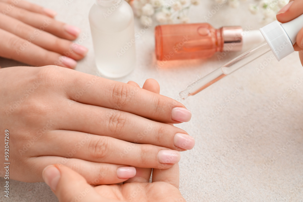 Manicure master applying cuticle oil onto female fingernails on light background, closeup