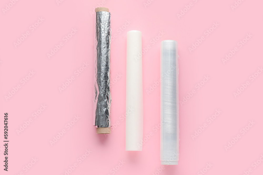 Rolls of aluminium foil, baking paper and food film on pink background