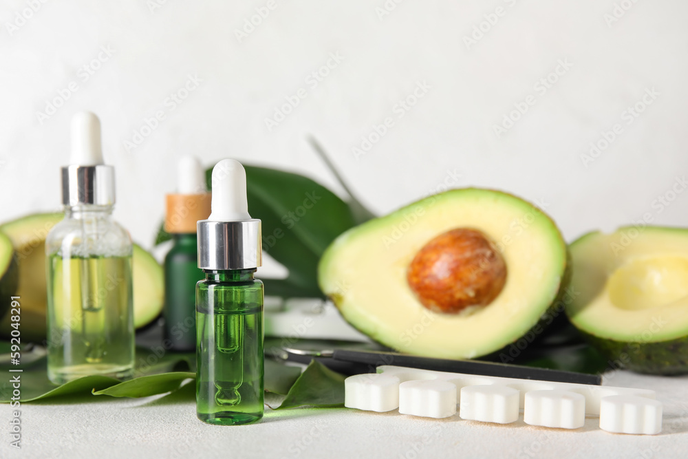 Composition with bottles of cuticle oil, manicure instruments, avocado and palm leaf on light backgr