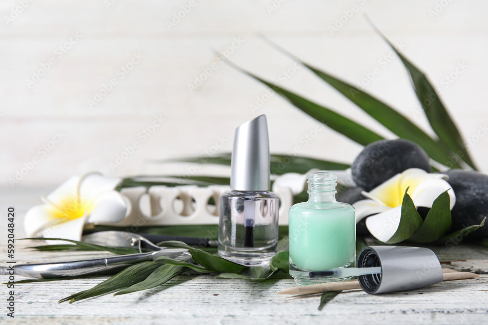 Composition with bottles of cuticle oil, manicure instruments, palm leaf and flowers on light wooden