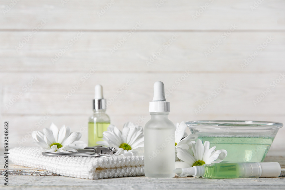 Composition with cuticle oil, manicure instruments and chamomile flowers on light wooden background