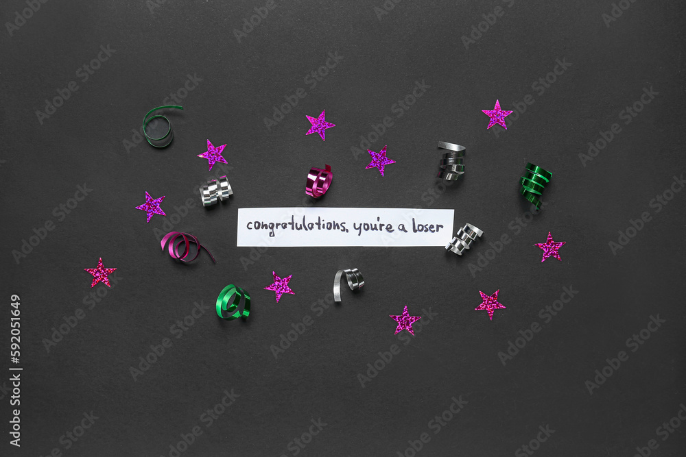 Paper with text CONGRATULATIONS YOURE A LOSER, stars and serpentine on dark background