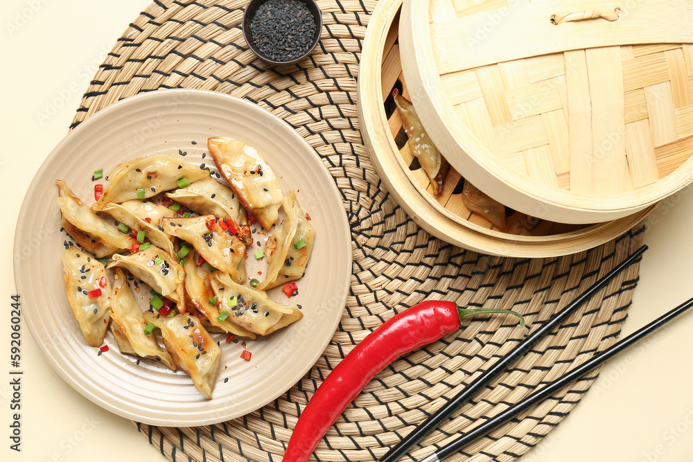 Plate with tasty Chinese jiaozi, red chili pepper and bamboo steamer on beige background