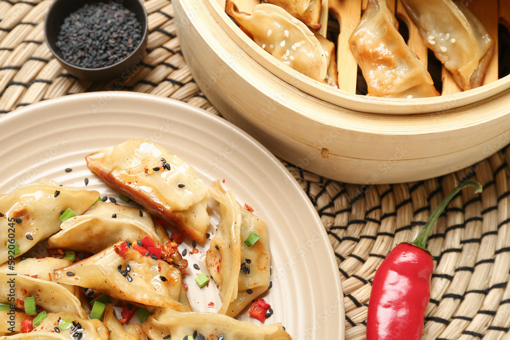 Plate with tasty Chinese jiaozi, red chili pepper and bamboo steamer on table